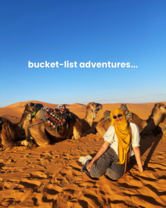 A photo of a woman in front of camels in the Sahara desert